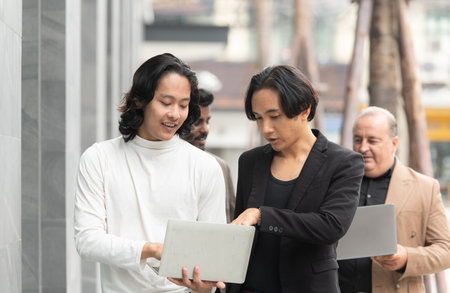 Group of business people walking and working on laptop computer in side of modern office building. Multiethnic group of business people using digital devices outdoor.の写真素材