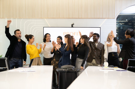 A group of multiracial businesspeople hands raise to celebrate success in front of the meeting room,...