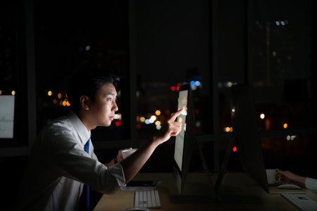 Young Asian broker international stock traders working at night in office using computer and thinking.の写真素材