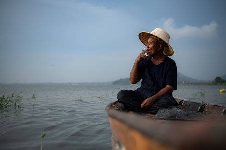 A fisherman relaxes in a boat on the lake while smoking.の写真素材