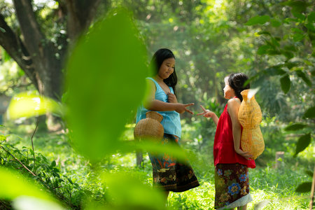 Two girls Asian women with traditional clothing stand in the rainforest. They had fun playing together before assisting Grandpa in catching fish in a nearby lake.の写真素材