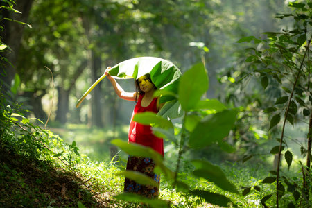 Little asian girl in red dress holding fishing equipment in the forest, Rural Thailand living life conceptの写真素材
