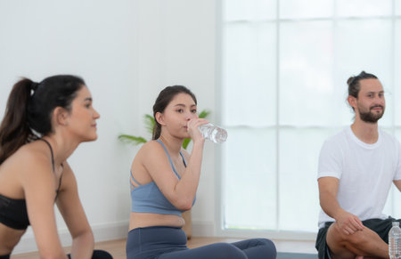 A group of female and male athletes sitting rest on yoga mats and drinking water. They are looking at each other and smilingの写真素材