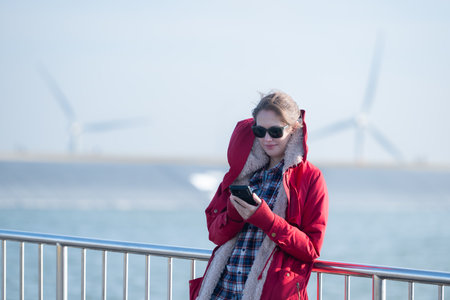 On the background of windmills, A young woman in a red jacket is enjoying her winter vacation.の写真素材