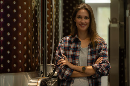 Portrait of a young woman standing in her winery with her arms crossed.