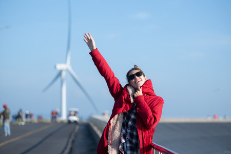 On the background of windmills, A young woman in a red jacket is enjoying her winter vacation.の写真素材