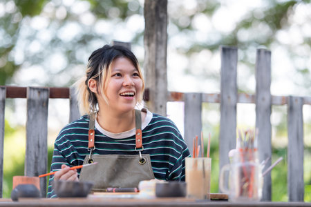In the pottery workshop, Asian woman is engaged in pottery making and clay painting activities.の写真素材
