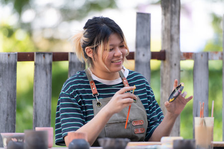 In the pottery workshop, Asian woman is engaged in pottery making and clay painting activities.の写真素材