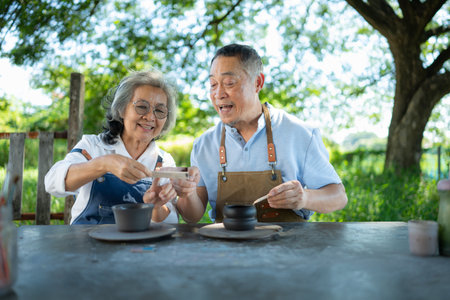 In the pottery workshop, an Asian retired couple is engaged in pottery making and clay painting activities.の写真素材