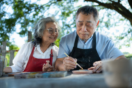 In the pottery workshop, an Asian retired couple is engaged in pottery making and clay painting activities.の写真素材