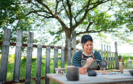 In the pottery workshop, Asian woman is engaged in pottery making and clay painting activities.
