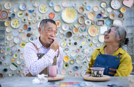 In the pottery workshop, an Asian retired couple is engaged in pottery making and clay painting activities.の写真素材