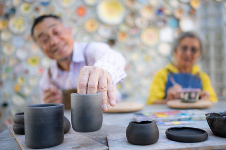 In the pottery workshop, an Asian retired couple is engaged in pottery making and clay painting activities.の写真素材