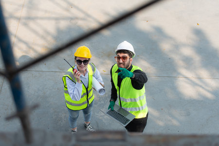 Overhead view on a building site, an engineer and architect are discussing on a laptop.