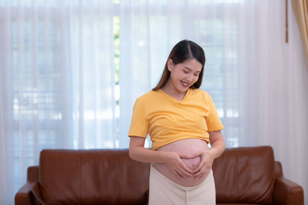 A pregnant woman feels happy at home while taking care of her baby in the womb. Young mother showing...