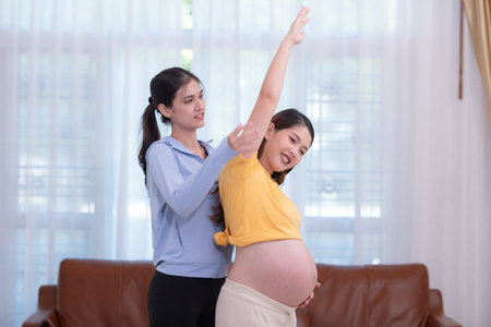Happy Asian pregnant woman with yoga teacher teaching pregnancy yoga in her living room.の写真素材