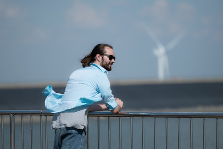 Young man relaxing by the wind turbine on the lakeの写真素材