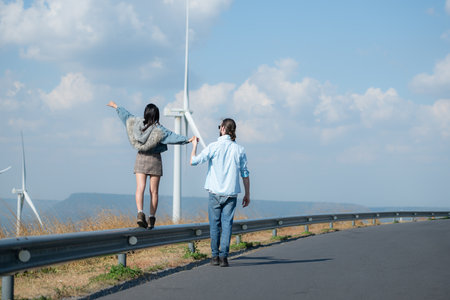 Back view of young couple walking on the road with wind turbines in backgroundの写真素材