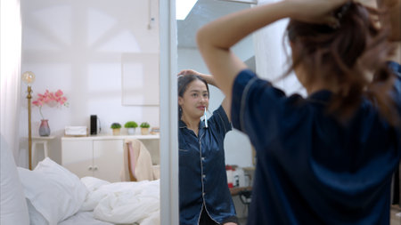 Asian young woman in a blue pajama is brushing her teeth in front of the mirror before taking a showerの写真素材