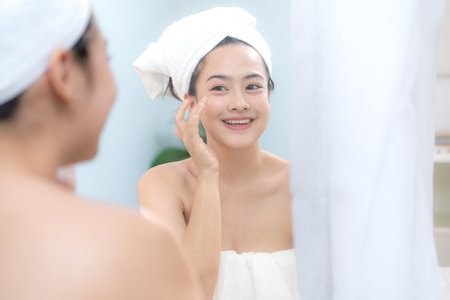 Asian young woman with towel wrapped on head and body applying makeup after shower, Morning beauty routine before workの写真素材