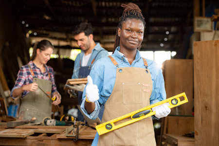 Portrait of carpenter female worker standing in front of colleague in workshopの写真素材