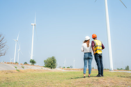 Back view of engineer and architect on construction site with wind turbines in backgroundの写真素材