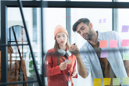 Multiethnic young business people brainstorming on a project by writing on the glass wall in the...