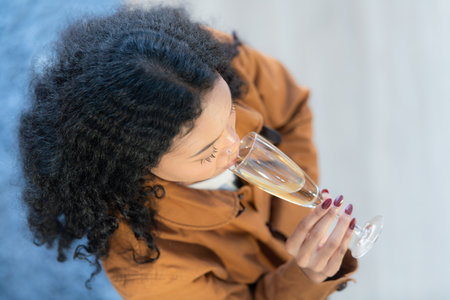 Happy young woman with glass of champagne sitting on sofa at homeの写真素材