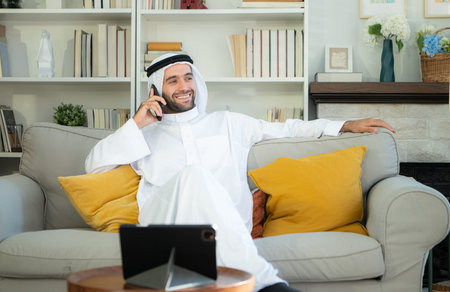 Portrait of a smiling Arabian man holding a glass of champagne and using mobile phone at home