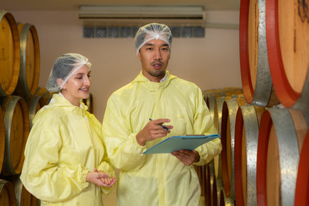 Mature female and male researchers and developers working in winery, Testing wine that has been...