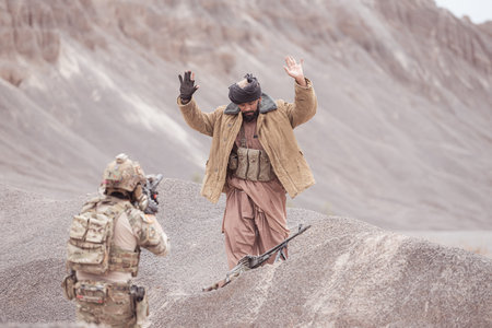 A Taliban soldier stands with a machine gun, Raise hands in surrender to the allied soldiers, In the...