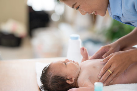Following a bath, a mother applies powder and dresses her tiny daughter.の写真素材