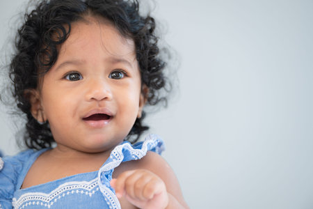 A little girl with a big smile sits on a bed in a sunny room, radiating happiness and joy