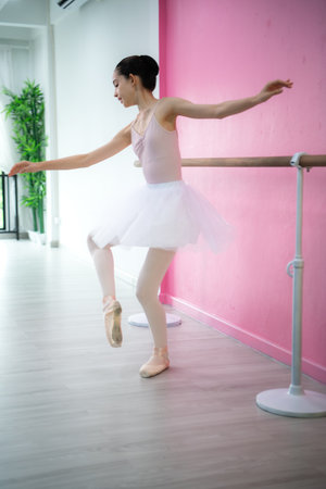 A girl ballet student practices ballet dancing at home with a pink and white backgroundの写真素材