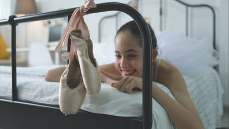 A girl ballet student look at the old ballet shoes hanging from the end of the bed, happy smileの写真素材
