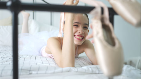 A girl ballet student look at the old ballet shoes hanging from the end of the bed, happy smileの写真素材