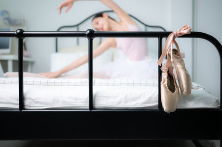 A girl ballet student warm up in bed and look at the old ballet shoes hanging from the end of the bedの写真素材