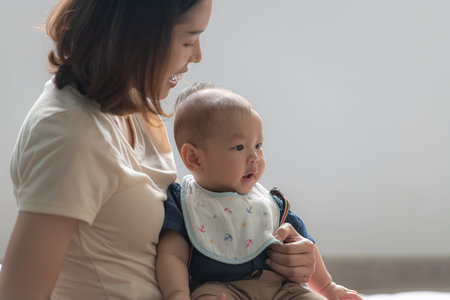 A tiny child smiling happily on the couch in the living room with mom