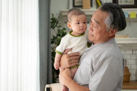 A tiny child smiling happily on the couch in the living room with grandfatherの写真素材