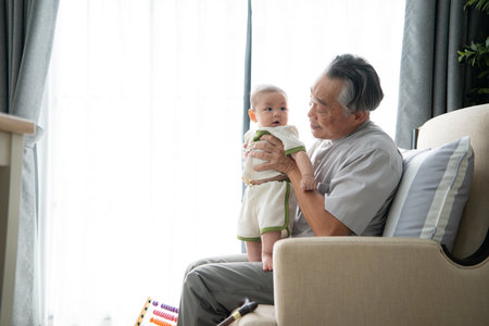 A tiny child smiling happily on the couch in the living room with grandfatherの写真素材