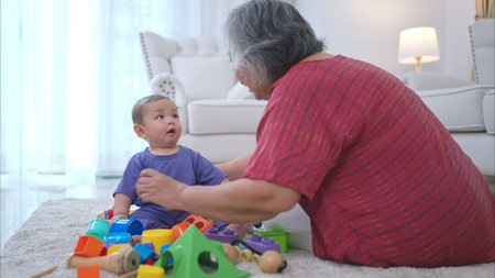 Grandmother and their little grandchild play happily in the living room of the houseの写真素材