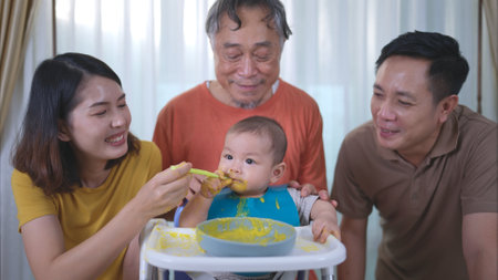A little child eating his first meal, parents and grandfather cheer excitedlyの写真素材