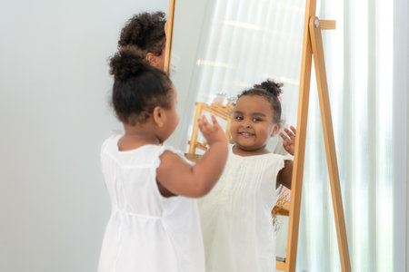 A little girl is looking at herself in the mirror in the dressing room of the houseの写真素材