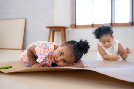 The older sister and younger sister sit on the floor and drawing together in the living roomの写真素材