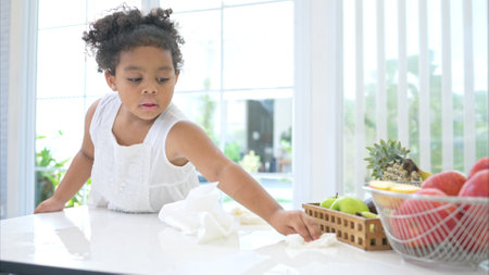 A tiny girl clean the table and floor after glass of milk spilled while drinkingの写真素材