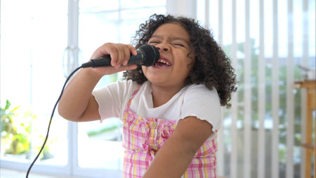 A tiny girl sits on a toy table, clutching a microphone, and sings cheerfully in the living roomの写真素材