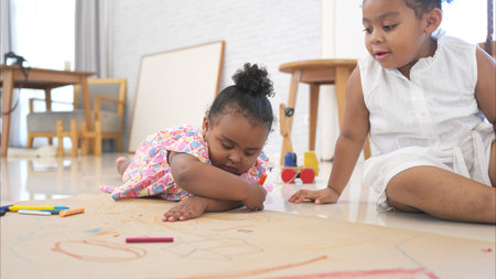 The older sister and younger sister sit on the floor and drawing together in the living roomの写真素材