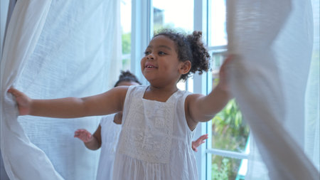 A tiny girl plays hide-and-seek with drapes in her bedroomの写真素材