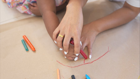 On a holiday, A mother and her little daughters sit on the floor and drawing hand in the paperの写真素材