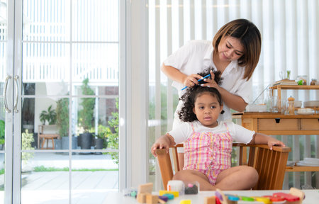 The mother helps her daughter get ready and ties her hair to make it seem neatの写真素材